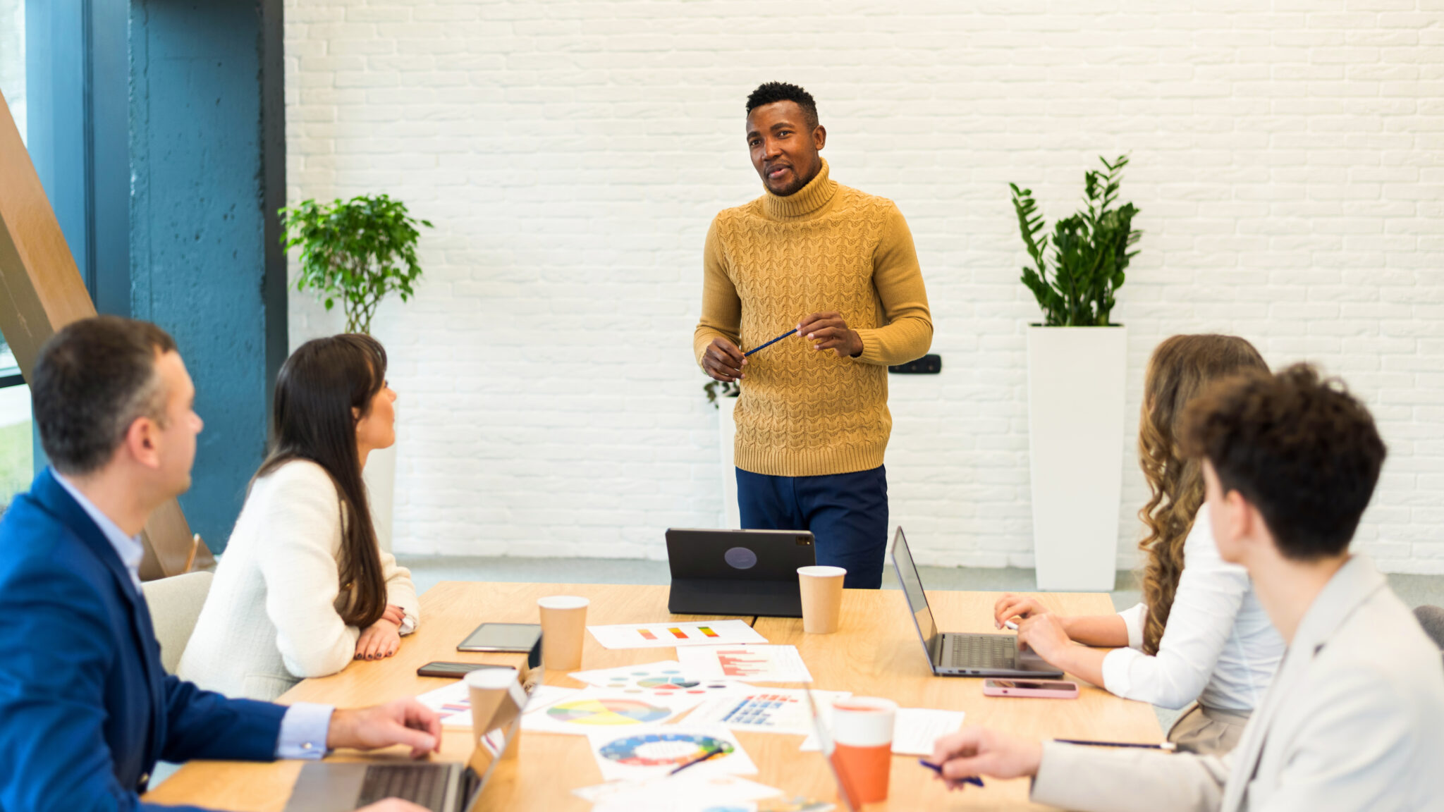 Professional leading a team meeting, demonstrating effective leadership communication skills, engaging colleagues around a conference table with laptops and documents, fostering collaboration and peak performance.